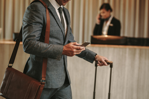 Cisco Meraki für das Hotelgewerbe Ein Mann mit Gepäck steht an der Rezeption und schaut auf sein Mobiltelefon